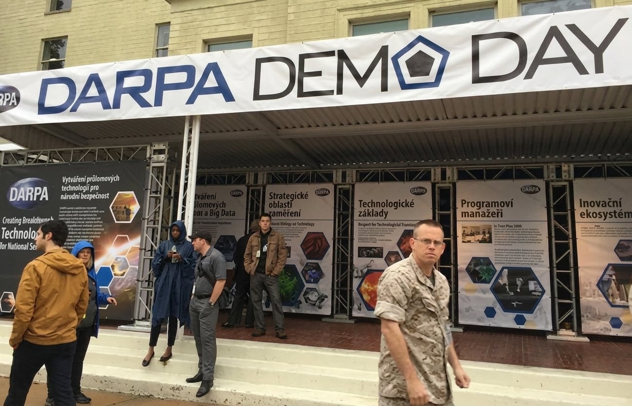 Konferenční stánky s nápisem nad nimi "DARPA Demo Day"