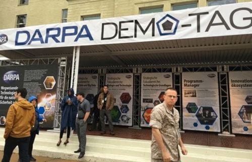 Bild von Ausstellungsständen auf einer Konferenz mit einem Banner, auf dem "DARPA Demo Day" steht