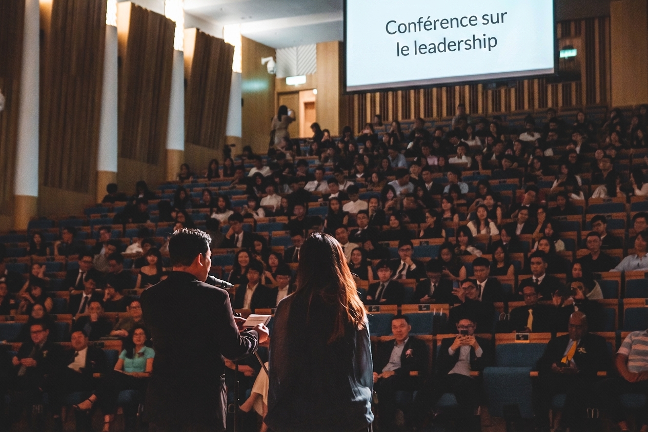 Deux personnes sont sur scène et s'adressent à un amphithéâtre rempli de centaines de personnes