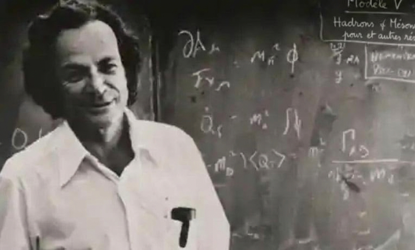 Richard Feynman se tient devant un tableau noir sur lequel sont inscrites des équations mathématiques.