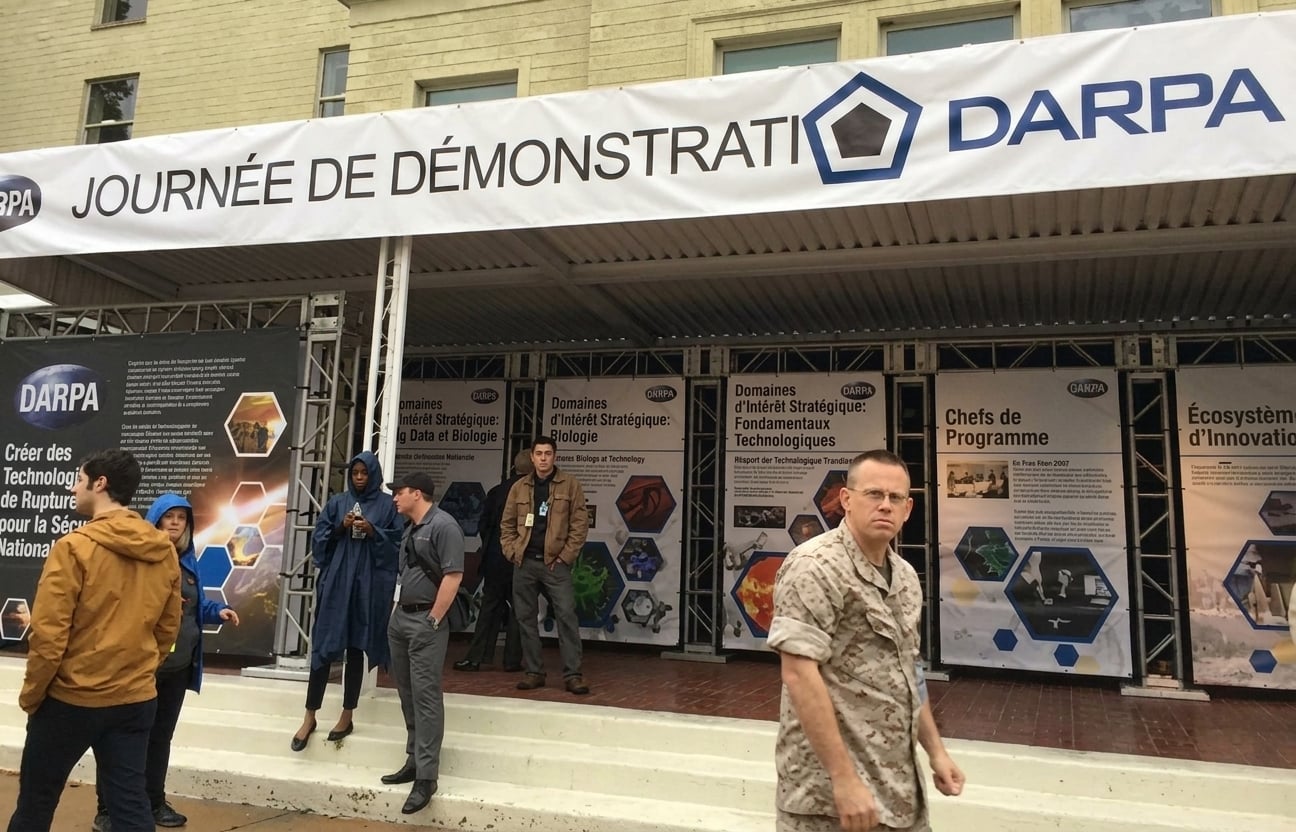 Image des stands d'exposition de la conférence avec une bannière au-dessus de laquelle on peut lire « DARPA Demo Day » (Journée de démonstration du DARPA)