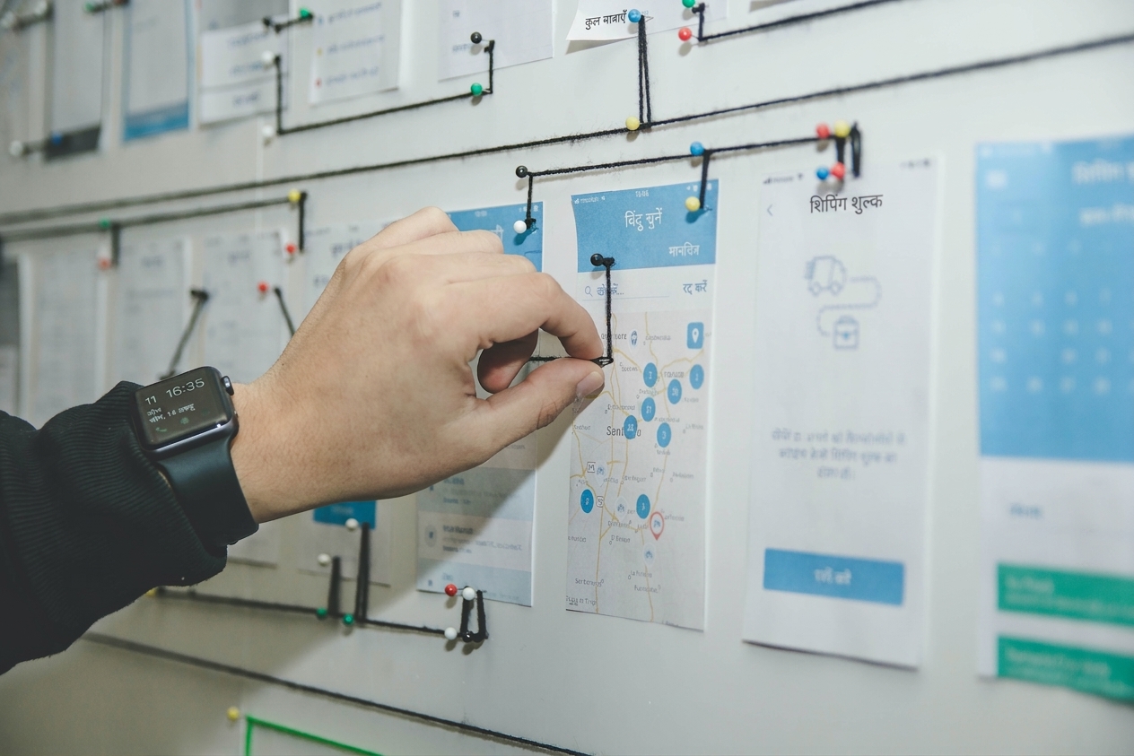 एक व्यक्ति कार्ड, धागे और पिन से बुलेटिन बोर्ड पर स्टोरीबोर्ड बनाता है