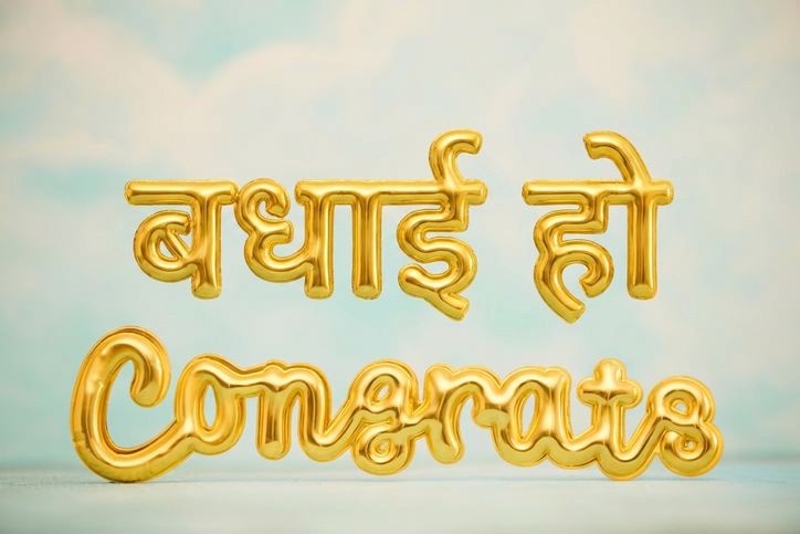 नीले आसमान में "congrats" वाले सुनहरे गुब्बारे