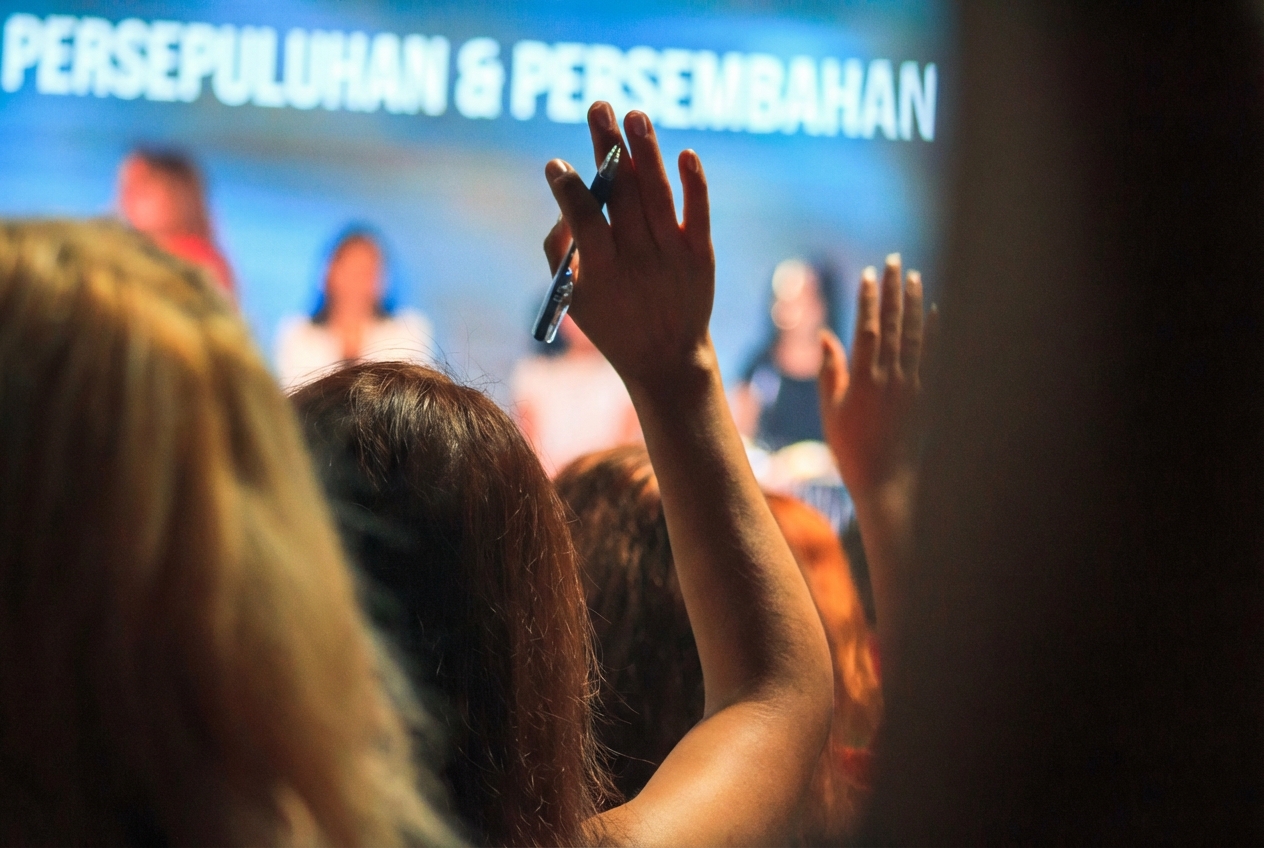 gambar orang di antara audiens yang mengangkat tangan untuk mengajukan pertanyaan kepada panel