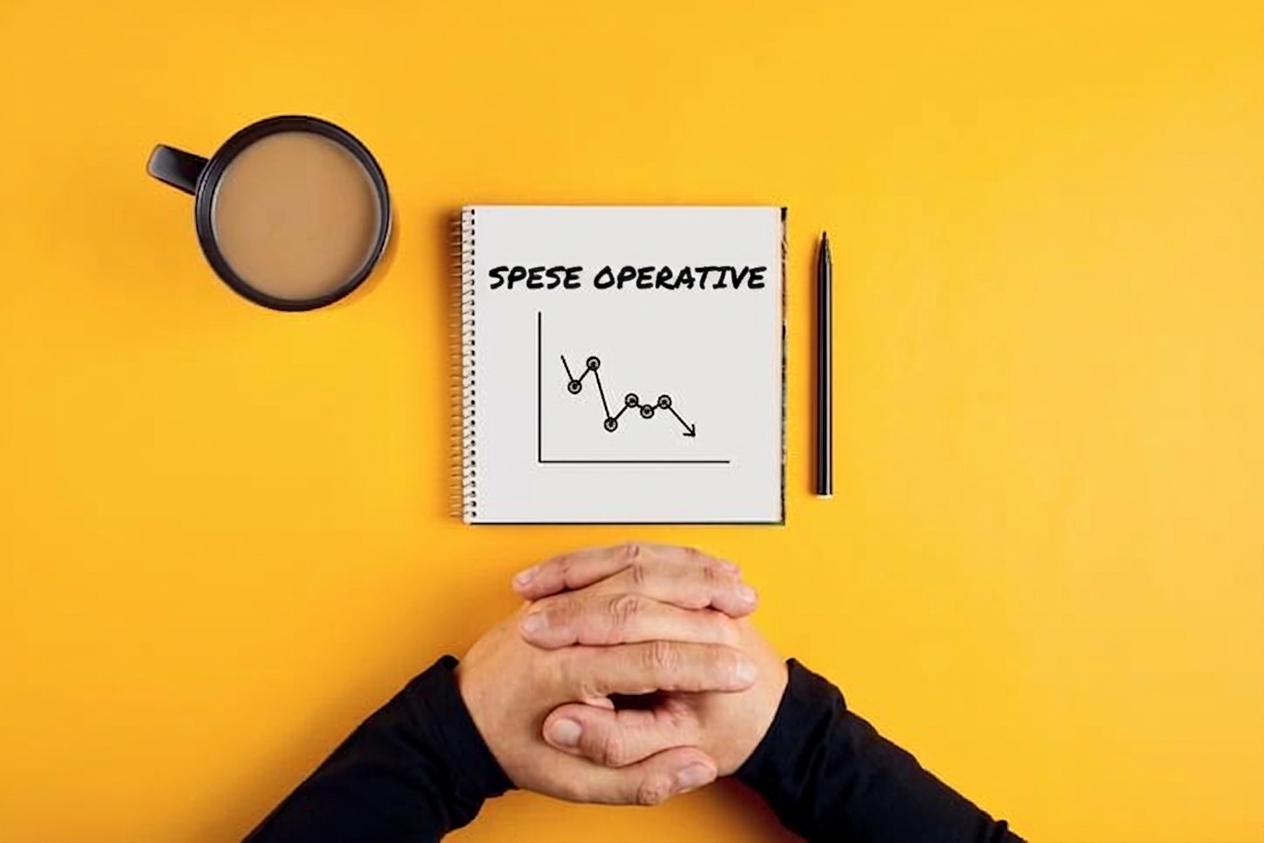 Immagine di un quaderno che mostra spese operative in calo, con una tazza di caffè e le braccia di un uomo