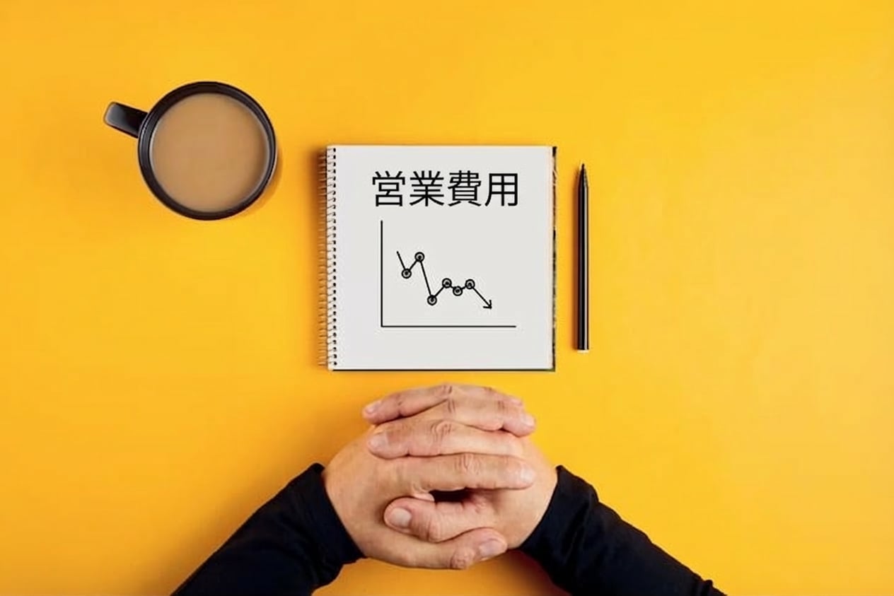 運営費の減少を示すノート、コーヒーマグ、男性の腕