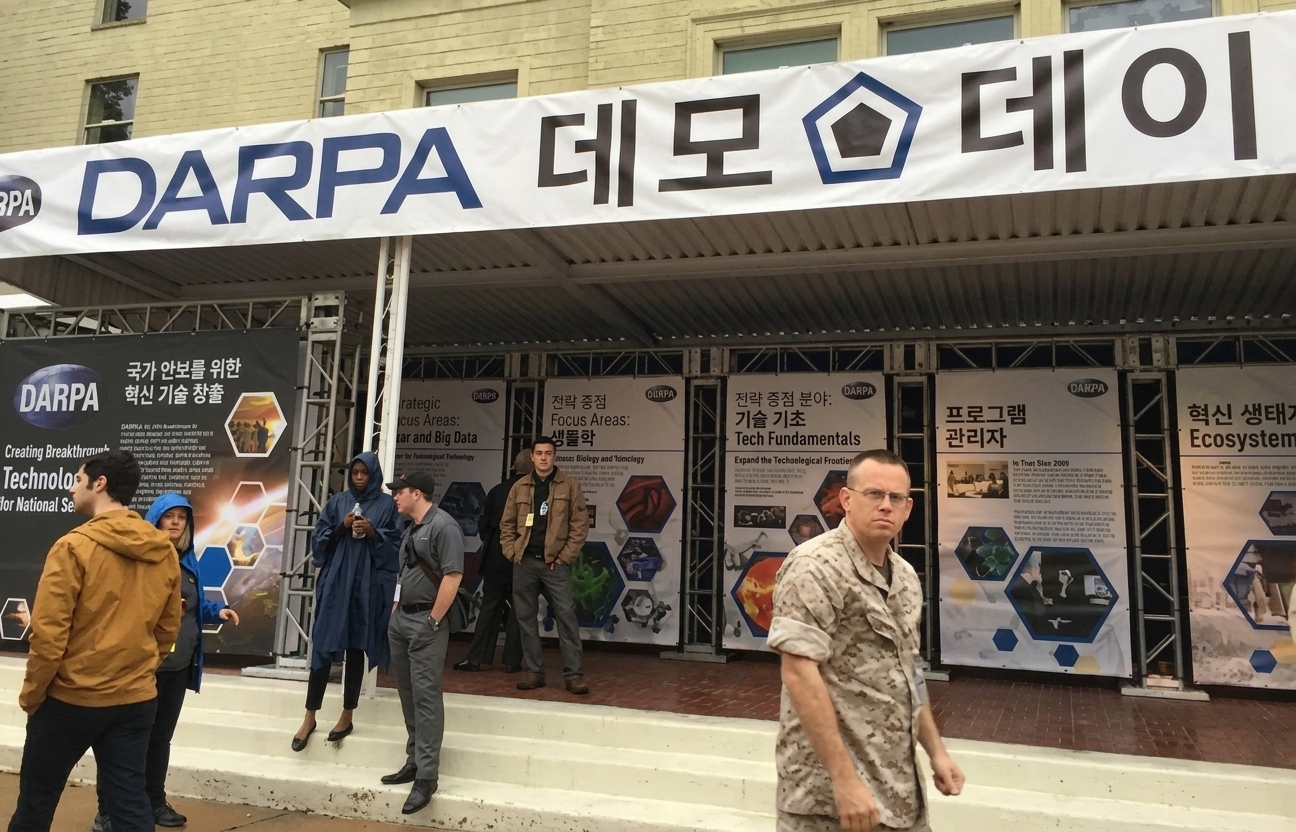 컨퍼런스 전시 부스와 그 위에 'DARPA 데모 데이'라고 적힌 배너가 보이는 이미지