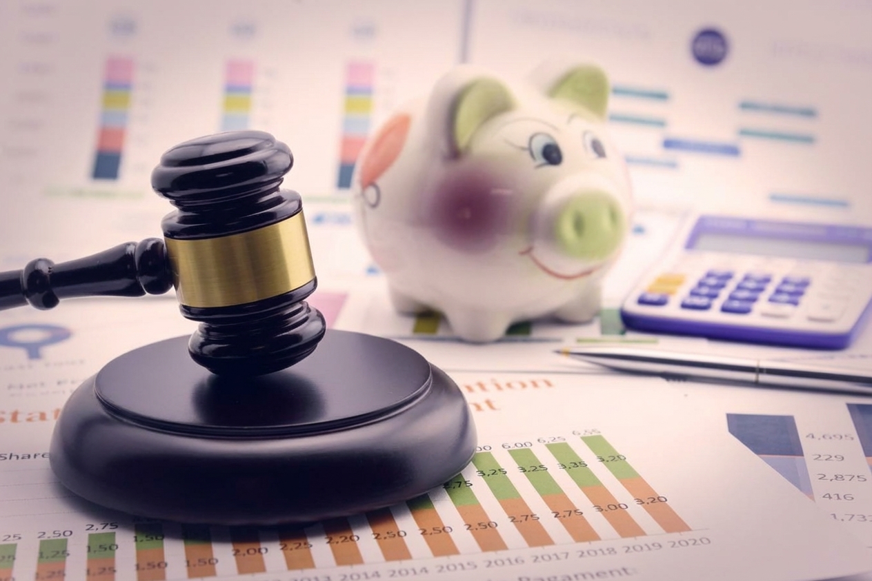Um martelo de juiz ao lado de um cofrinho e uma calculadora, representando regulações financeiras