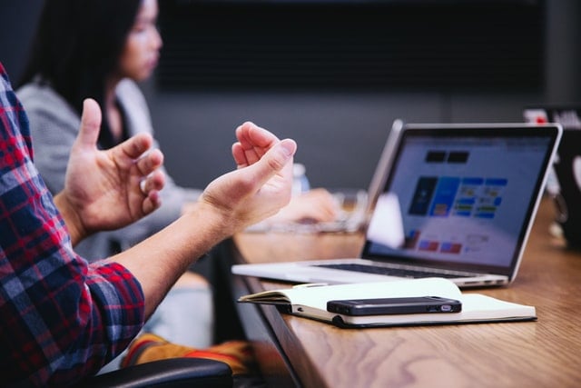 Two hands with a gesture of explaining and a computer displaying a slide