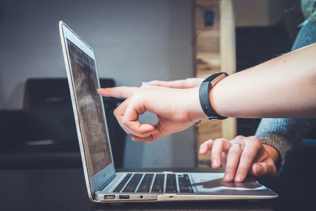 Two hands and a finger pointing to the computer screen