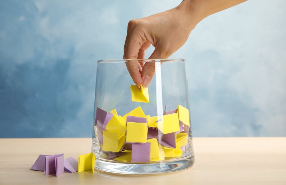 A hand picking a folded piece of paper out of a raffle jar.
