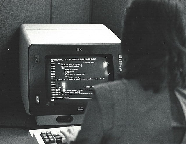 A black-white picture of a single person in front of a 1980 computer