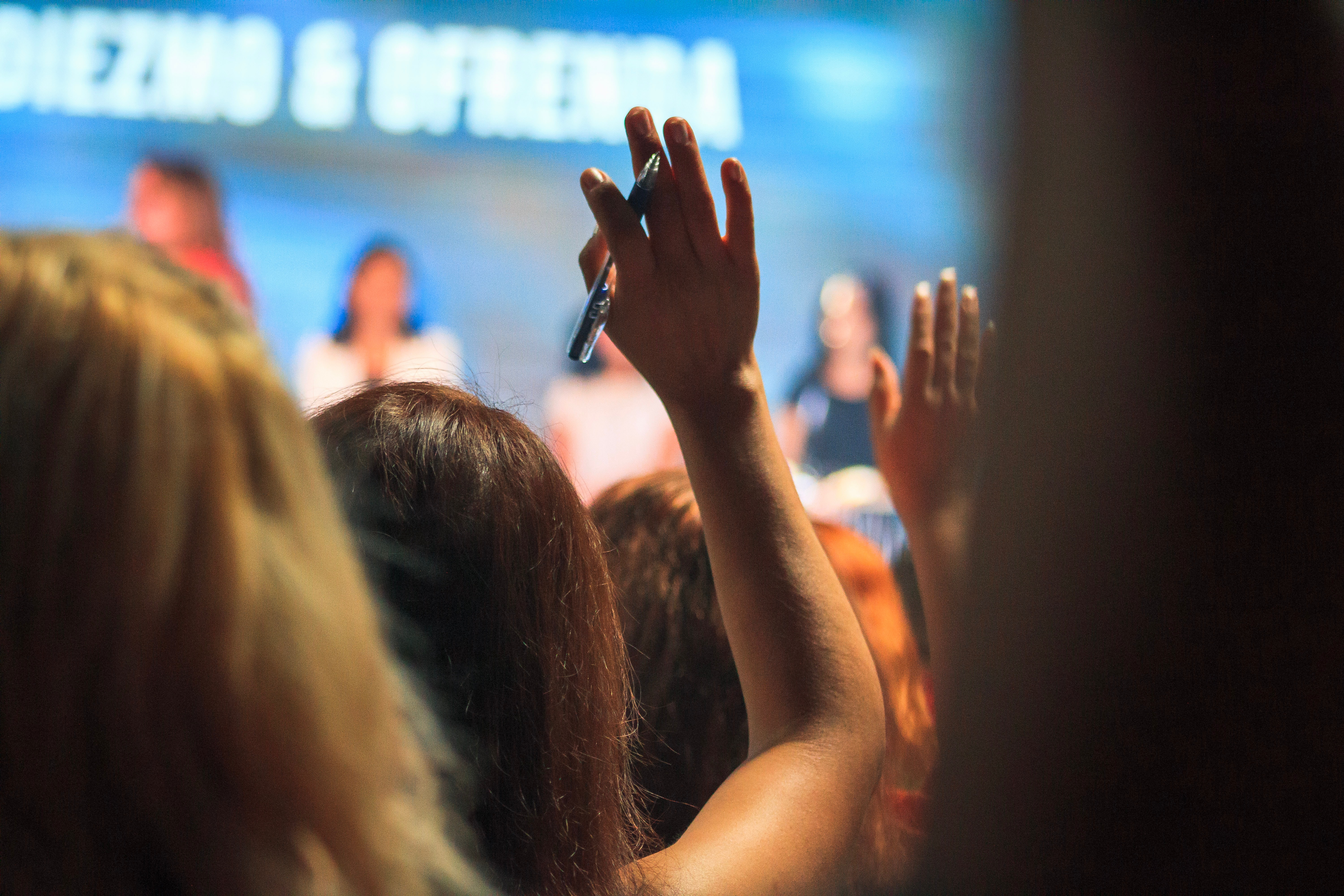picture of someone in an audience raising their hand to ask a panel a question