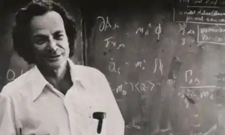 Richard Feynman is standing in front of a blackboard with math equations