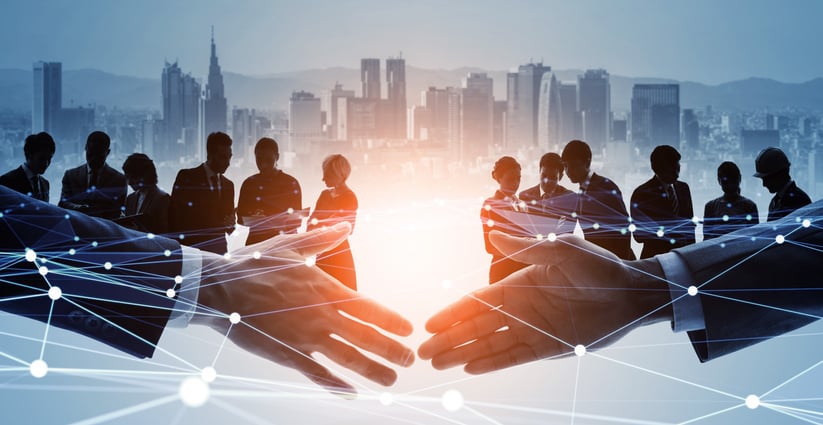 Shaking hands in front of a group of people to illustrate collaboration