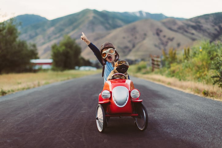 A boy riding with a dog in a car pointing with his index finger to indicate success