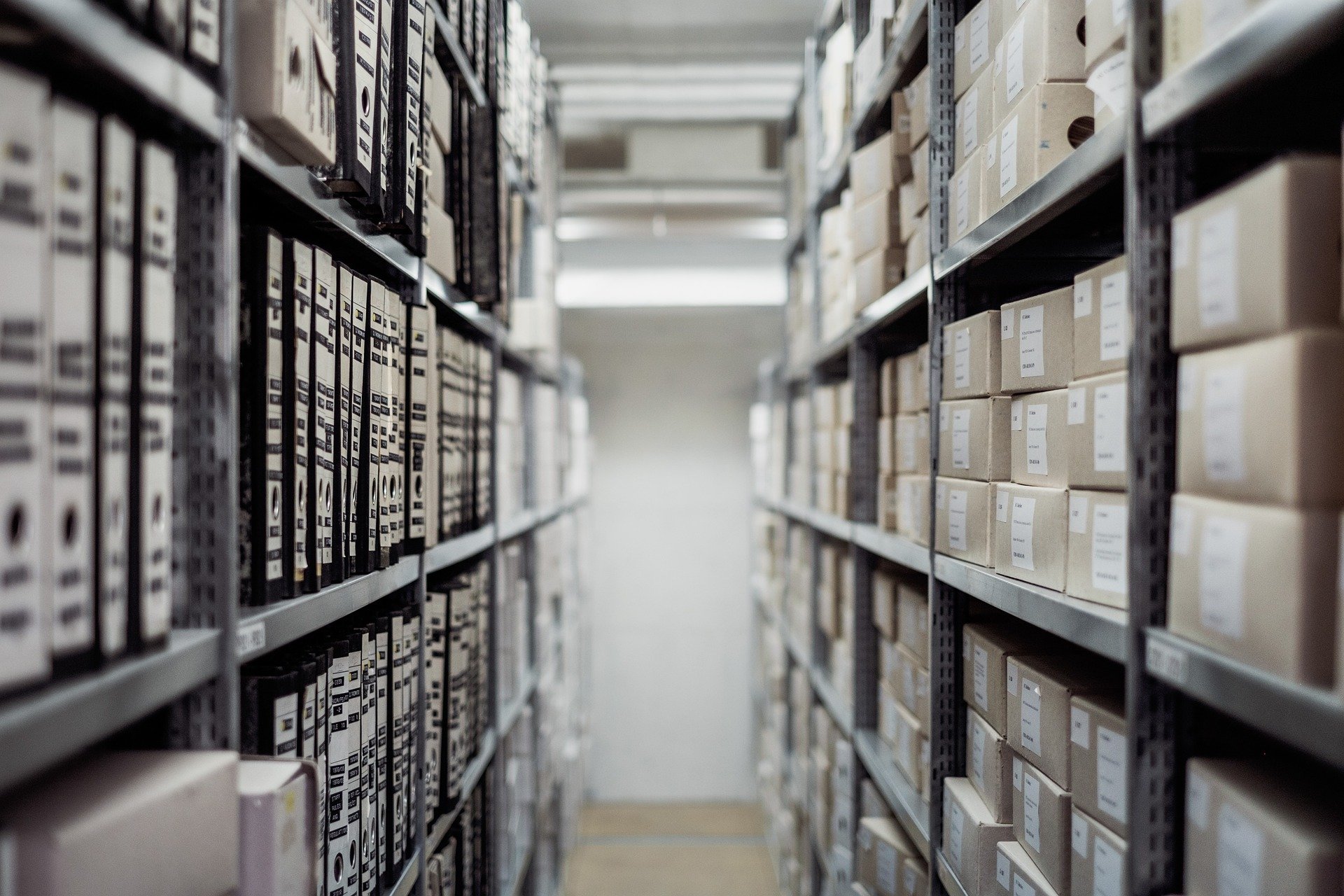 Photo shows an archive with shelves filled with records and boxes representing file storage.