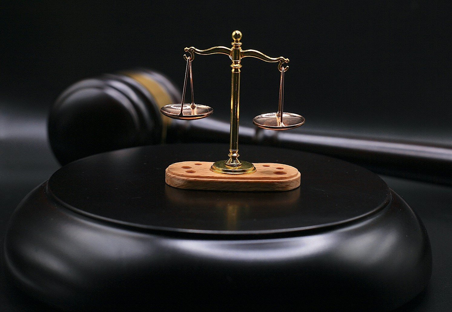 Picture featuring balance scales, with a gavel in the background.