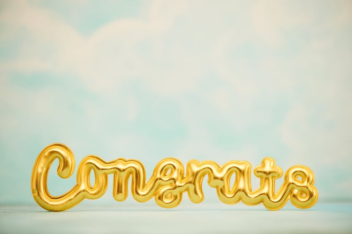 gold balloons against blue sky saying congrats