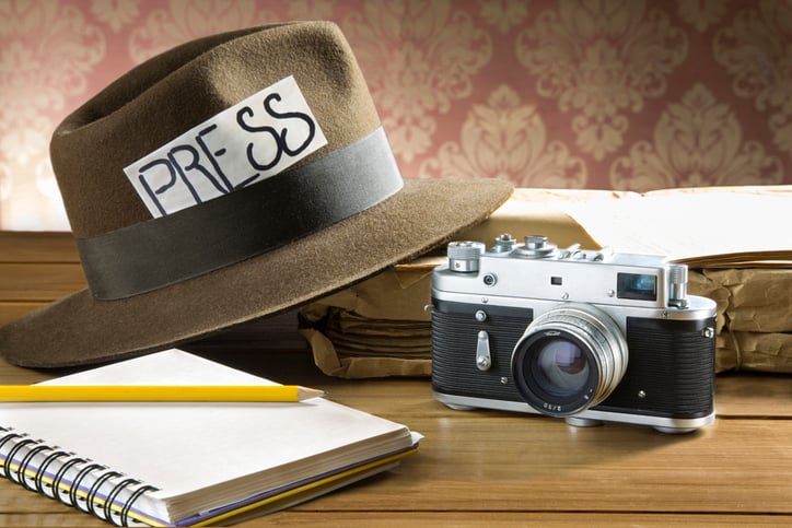 Picture of a camera, notepad, and a hat with a press tag