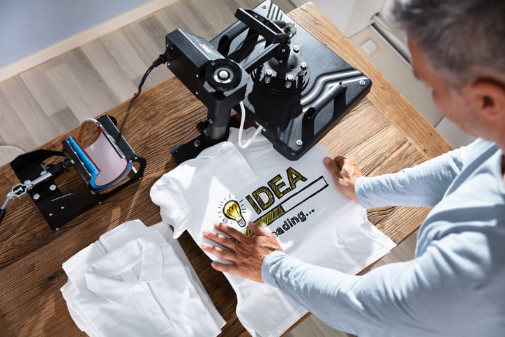 A man holding a t-shirt in a machine that is printing on it
