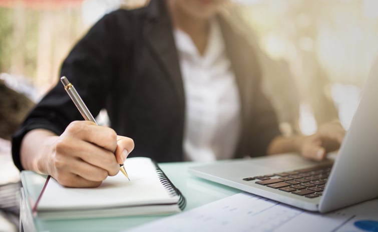 Person writing in a notebook and checking a computer