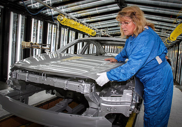 A factory line worker installing the hood of a vehicle
