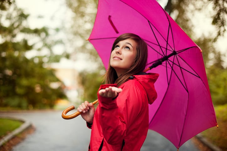 Image of a woman with a pick umbrella checking if it is raining.