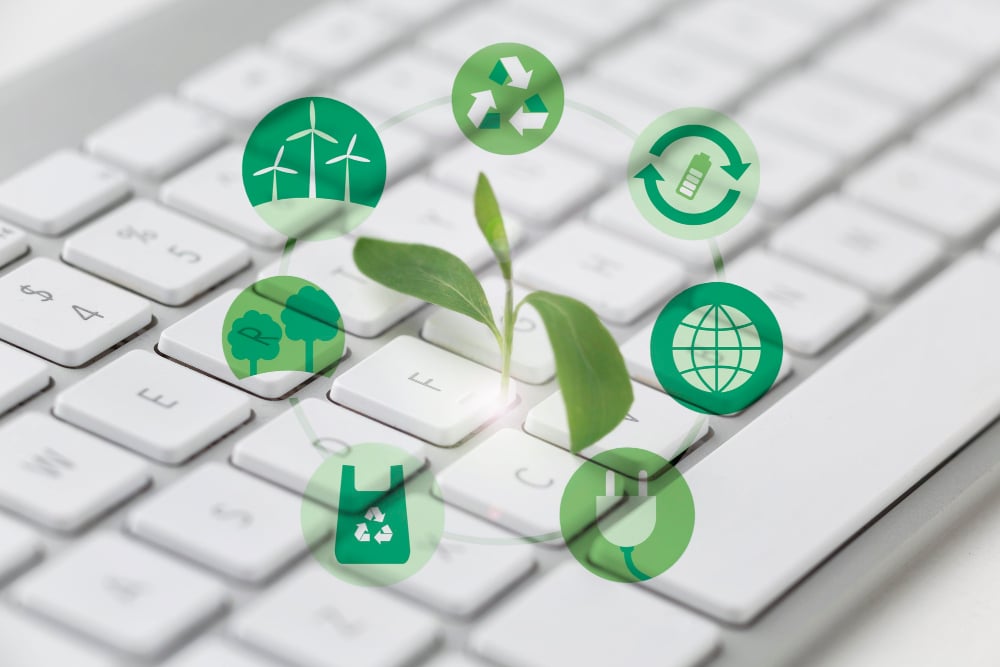 7 circular symbols of windmills, reusable bags, trees, recycle, battery recycle, a plug and the globe in the foreground. A white laptop keyboard in the background.