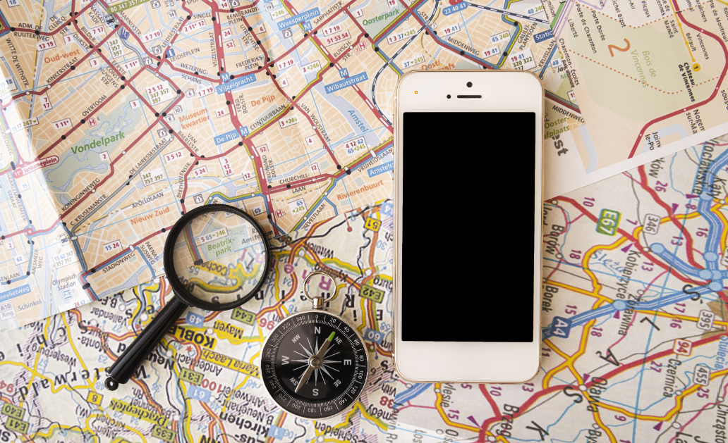 A mobile phone, compass, and a magnifying glass on a map.