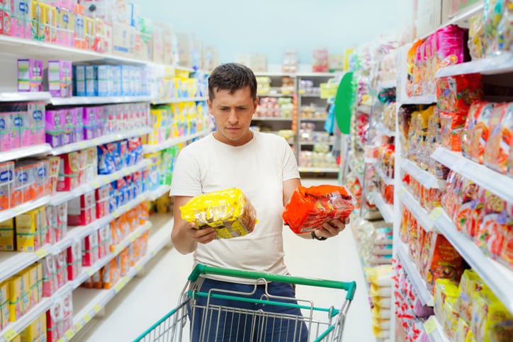 Man looking at two products in the supermarket that appear the same apart from the color of the packaging