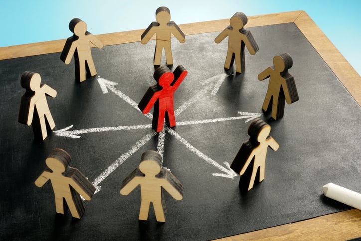 Image showing wooden figures in a circle, with one different colored figure in the middle