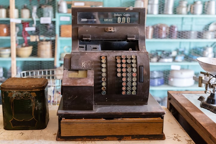 A old and rusty cash register machine sits on a shop counter.