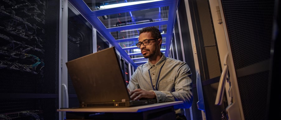 An engineer works on his laptops surrounding by stacks of computers.
