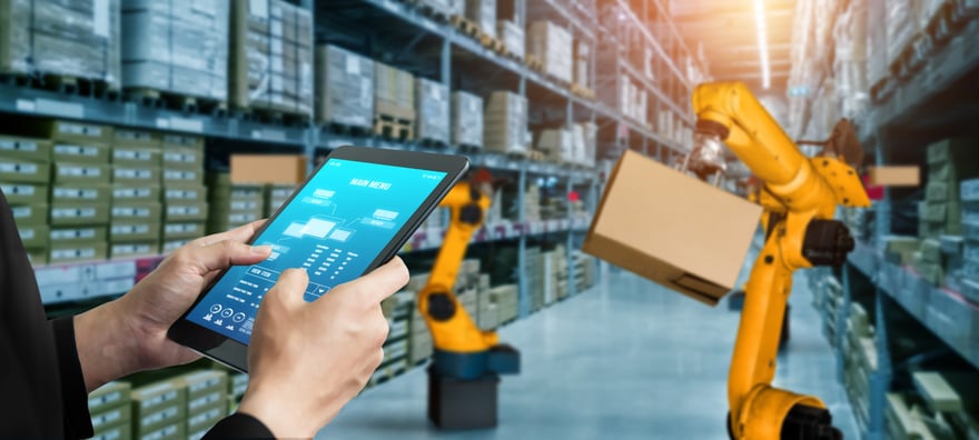 A person uses a tablet device to view analyses and visualizations while robotic arms place items on shelves in a warehouse.