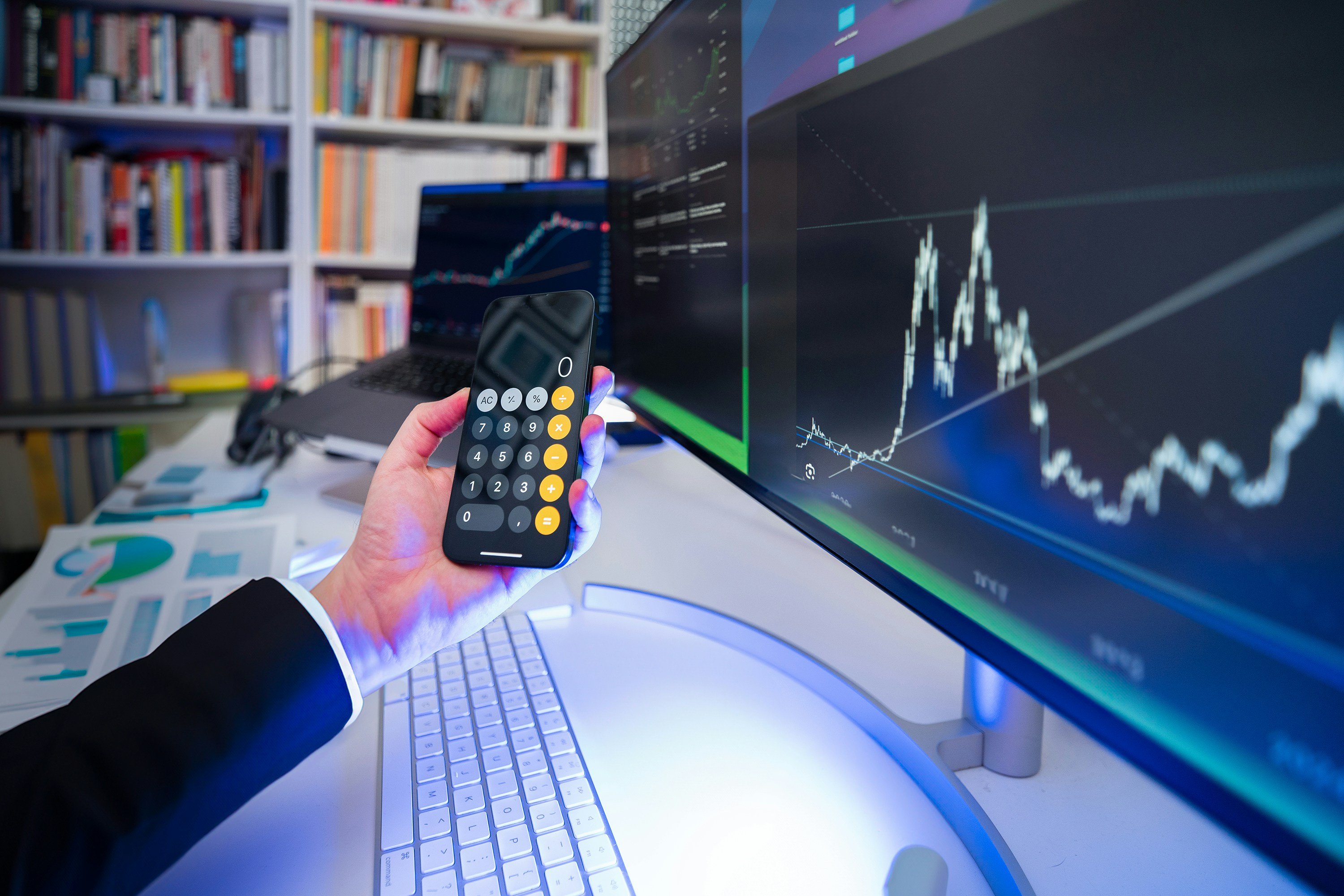 A hand holding a calculator in front of a screen with a line graph